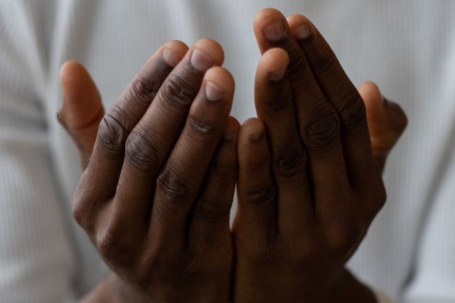 Selective focus of crop anonymous African American man wearing white turtleneck praying with open hands